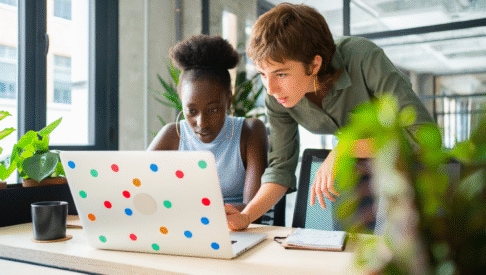 Zwei Mitarbeiterinnen sind im Büro am Schreibtisch und schauen auf denselben Laptop